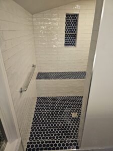 Walk in shower with blue hexagon tiles and white subway tiles and bench with niche.