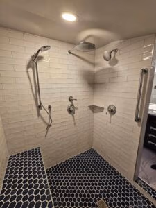 Walk in shower with blue hexagon tiles and white subway tiles and chrome shower heads.