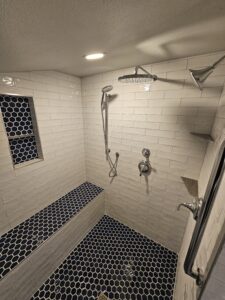 Walk in shower with blue hexagon tiles and white subway tiles and chrome shower heads.