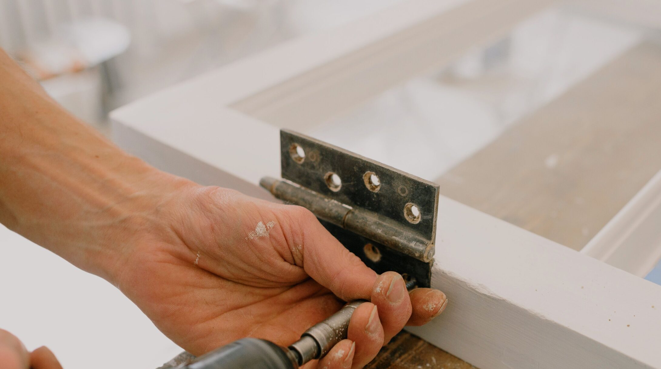 worker drilling metal hinge on white window frame during house renovation